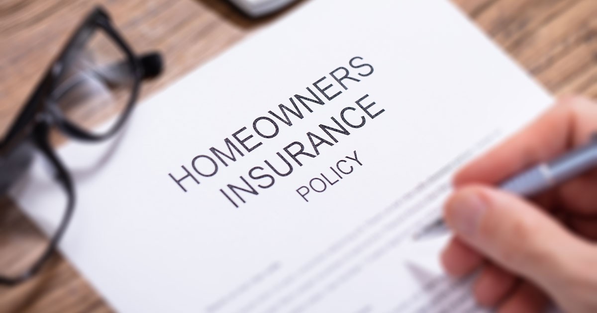 Close-up of a homeowners insurance policy document with a hand holding a pen.