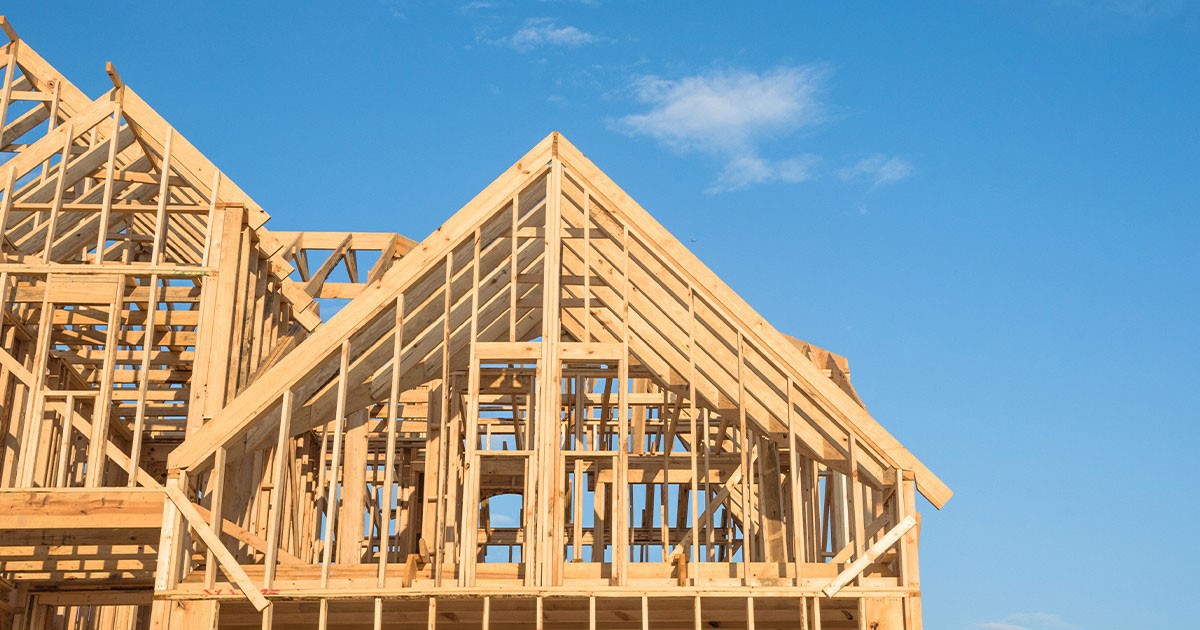 Wooden framework of a house under construction against a clear blue sky.