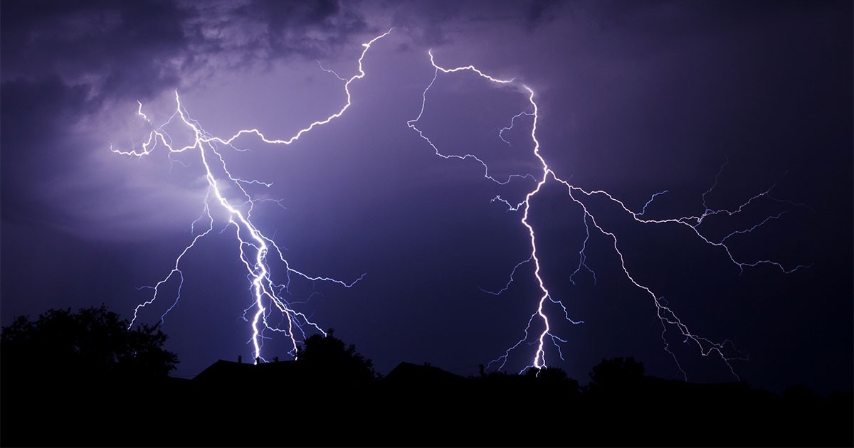 Multiple lightning bolts against a dark night sky with silhouetted trees and rooftops.