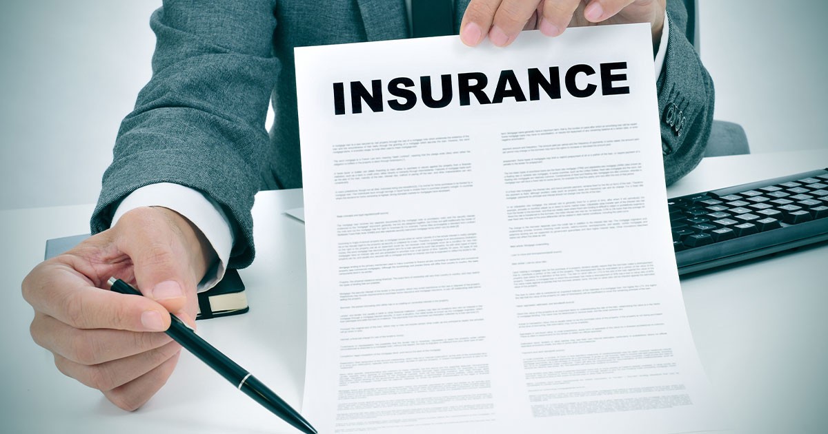 Person holding an insurance document with a pen in an office setting.