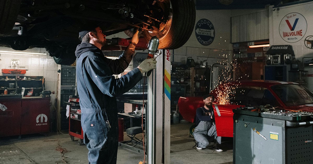 Mechanics working in an auto repair shop with tools and signs in the background. Photo by cottonbro studio via Pexels