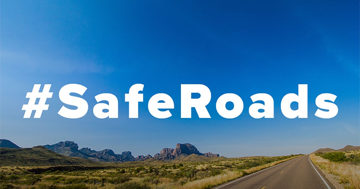 Desert road under a blue sky with #SafeRoads text